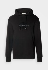 Zwarte hoodie van zacht materiaal, met een voorzak, een trekkoordcapuchon en een logo tekst "Calvin Klein Jeans" op de borst.