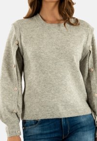 Maglione grigio chiaro realizzato in materiale morbido, con collo a coste e maniche lunghe, arricchite da bottoni decorativi lungo i lati.