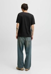 Sort bomulds t-shirt kombineret med oversized, falmede blå denim jeans. Outfittet har en afslappet pasform, synlige sømme og et minimalistisk design.