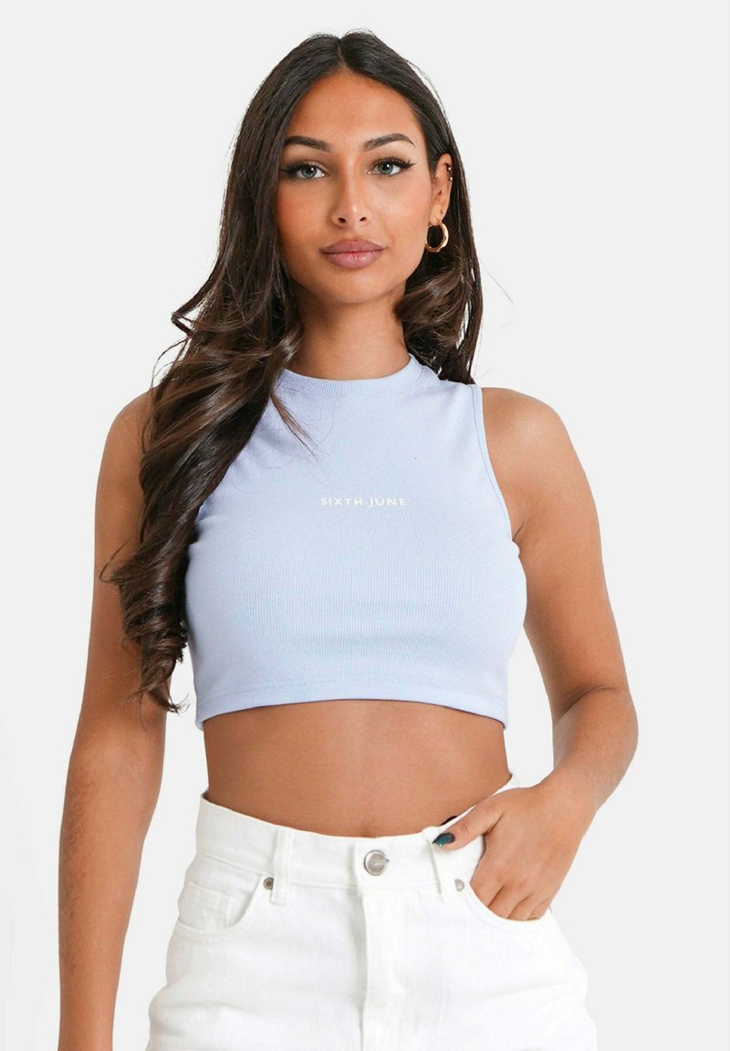 Top corto de canalé azul claro con un cuello alto, que presenta un pequeño logo dorado "SIXTH JUNE", combinado con pantalones cortos blancos de talle alto.