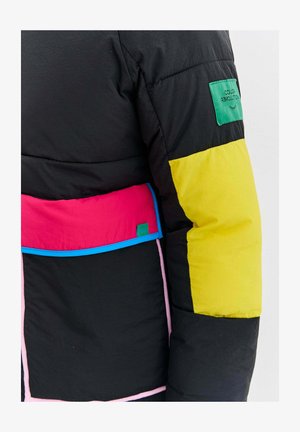 Czarna kurtka puchowa z jasnosłonecznym żółtym rękawem, różowymi i czerwonymi panelami, niebieskim wykończeniem oraz zieloną łatą z napisem "Kolorowa Rewolucja".