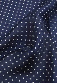 Tessuto navy con pois bianchi, caratterizzato da una superficie liscia e una leggera lucentezza. I pois sono distribuiti uniformemente su tutto il materiale.