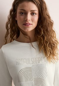 Weißer Sweatshirt mit dem Text "ARTFUL SHAPES" in einer eleganten Schriftart, versehen mit einem linearen Muster, das in einem dezenten Silberton gedruckt ist.