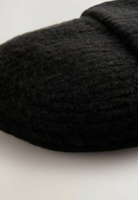 Schwarzer Filzschuh mit runder Form, strukturiertem Oberflächen und einer subtilen Naht entlang der oberen Kante. Aus weichem, flauschigem Material gefertigt.