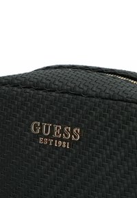 Borsa cosmetica nera intrecciata con una texture liscia, dotata di un logo dorato "GUESS EST 1981" e chiusura con zip nella parte superiore.