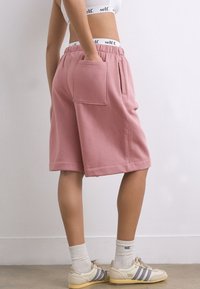 Shorts roses en mélange de coton avec une coupe ample, des poches latérales et une poche arrière. Portés avec des chaussettes blanches et des baskets aux couleurs claires avec des rayures.