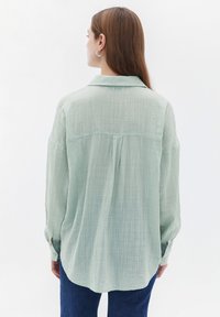 Lichtgroene, gestructureerde blouse met een kraag, lange mouwen en een ronde zoom. Bevat achterste naaddetails en knopenmanchetten.