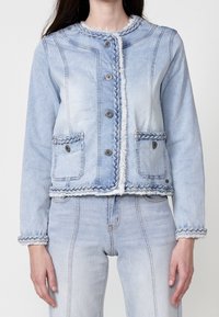 Light blue denim jacket with a braided trim, five buttons, frayed hem, and two front pockets. Features structured fit and long sleeves.