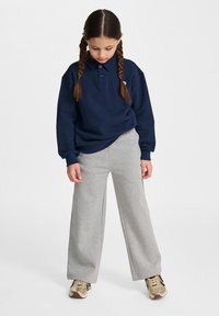 Marinblå tröja med krage och tre knappar, tillsammans med ljusgrå vida sweatpants. Sneakers är guld med svarta accenter.