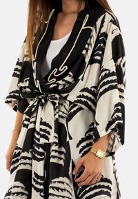 Bata al estilo kimono en blanco y negro con patrones de hojas de palma, mangas anchas y cintura ceñida con cinturón; hecha de tela ligera.