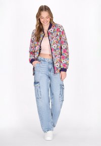 Bloemen bomberjack in levendige kleuren met ribbels aan de mouwen, gecombineerd met lichtblauwe oversized cargo-broeken met meerdere zakken.
