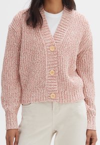 Vaaleanpunainen neulecardigan, jossa on V-nuora, pitkät hihat ja neljä suurta puulitukkaa edessä. Raitakangas ja ribattu hihansuu.