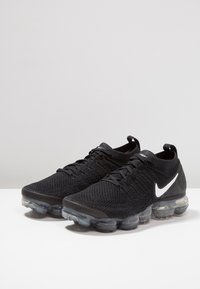 Chaussures de sport noires en matériau tricoté respirant avec une finition texturée, arborant un swoosh Nike blanc et une semelle à coussin d'air transparent.