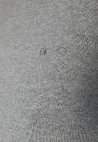 Tissu de pull en tricot gris avec une texture douce ; présente un petit logo "ck" noir brodé sur le devant.