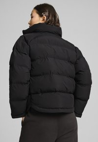 Sort pufferjakke med høj krave, quiltet design og cropped snit. Materialet ser glat og let skinnende ud med en let vægt.