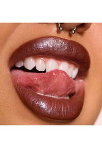 Nærbillede af læber med en glansfuld, dyb brun finish, der fremhæver en glat tekstur og en sølv septum piercing, med en delvist synlig tunge.