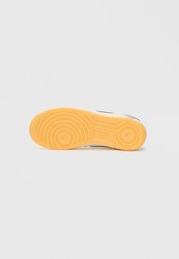 Sola de sapato com um desenho de piso circular. O borracha é laranja com padrões elevados para aderência, contra um fundo neutro.