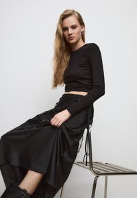 Črn dolg rokav krojena majica v kombinaciji z visokim pasom črne satenaste krila z detajli iz čipke in bleščic, obuta v črne škornje do kolen.