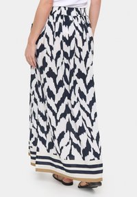 Maxi-rok van witte stof met een marineblauw abstract patroon. Heeft een tailleband en horizontale strepen aan de zoom in marineblauw en beige.