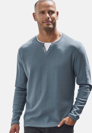 Langarm henleyshirt van zachtblauwe stof. Voorzien van een drieknoopsluiting, ronde halslijn en geribbelde manchetten. Glad tekstuur, geen patronen.