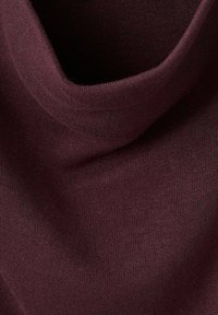 Primissimo piano di un morbido tessuto di maglia di colore viola scuro con una texture piegata, che mostra dettagli fini del filato e una superficie liscia.