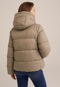 Kaki krāsas pūkains mētelis ar kapuci, kuram ir horizontālas quiltētas daļas un elastīgas aproces. Mīksts, izolējošs materiāls siltumam.