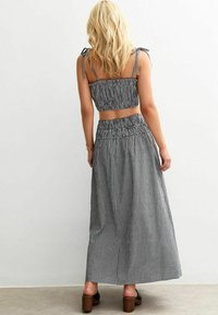 Black and white gingham crop top with elastic smocking, paired with a matching long skirt and tied straps. Flat sandals and light texture.