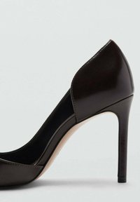 Zapato de tacón alto negro con acabado brillante, punta redonda y perfil lateral curvado. Presenta un tacón de aguja delgado y un interior beige.