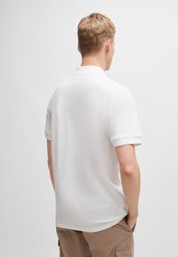 Bílá polokošile s krátkými rukávy, se standardním límečkem a měkkou strukturou. Jednoduchý design bez viditelných vzorů nebo akcentů.
