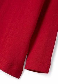 Roter Strickstoff mit einem strukturierten Muster aus kleinen Rauten. Die Kanten sind mit einem sauberen Saum verarbeitet und zeigen kurze Ärmel.
