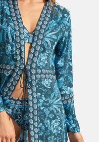 Turquoise bloemen badpak cover-up met een striksluiting, lange mouwen, ingewikkelde patronen en een textuurstof met contrasterende accenten.