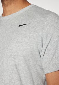 Camiseta de algodón gris con mangas cortas, que presenta un pequeño logo negro de Nike en la parte superior izquierda del pecho. Tela suave y texturizada.
