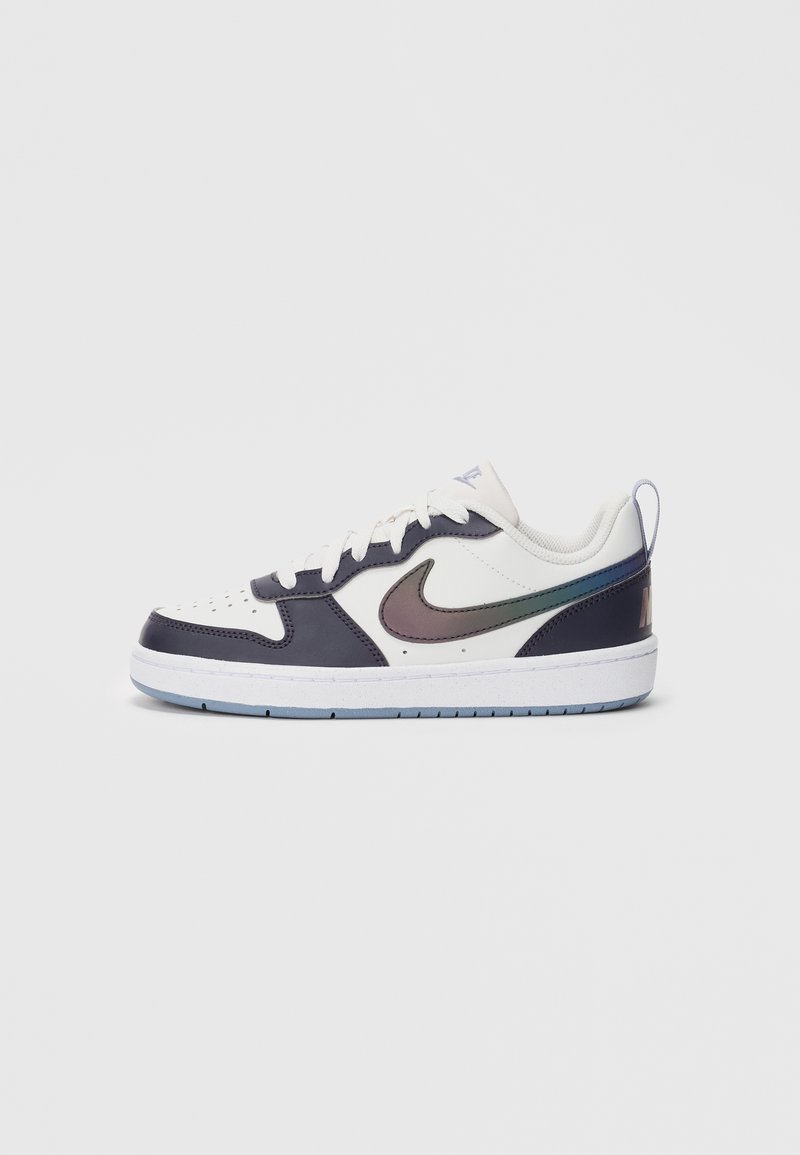 Tenis Nike cu aspect alb și negru, de tip low-top, cu swoosh iridescent, șireturi albe și talpă de un albastru deschis, prezentat din profil lateral pe un fundal alb.