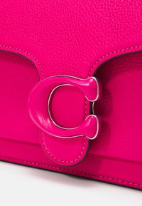 Pink leather handbag featuring a textured finish, a silver "C" hardware detail, and contrasting stitching. Close-up view of the clasp.