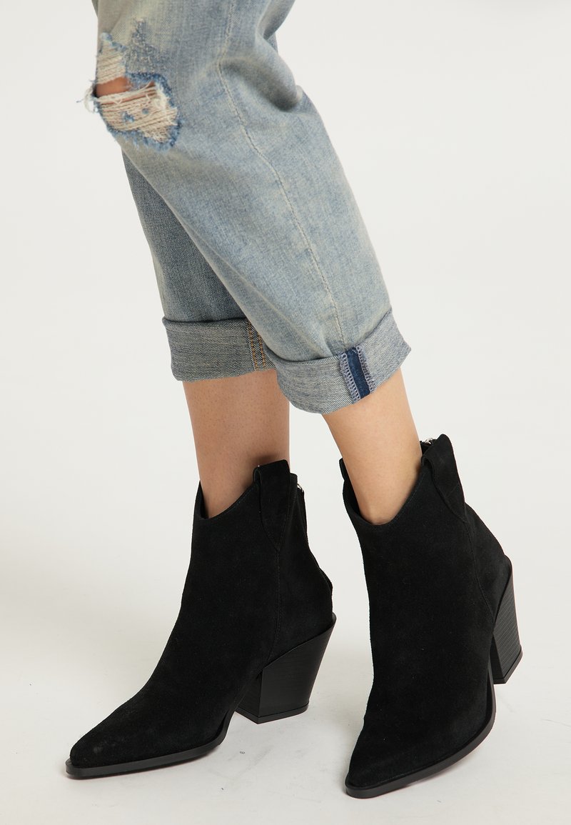 Stivali alla caviglia in suede nero con punta affilata, tacco a blocco alto e cerniera laterale. Indossati con jeans chiari distressed arrotolati.
