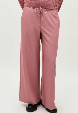 Miękkie różowe spodnie o szerokich nogawkach z ściągaczem w talii, noszone z czarnymi butami i pasującym różowym swetrem.