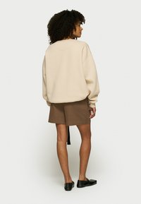 Sudadera beige de gran tamaño hecha de una tela suave, combinada con pantalones cortos marrones que presentan un detalle de lazo lateral. Zapatos planos negros completan el conjunto.