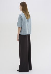 Giacca in denim oversize di colore azzurro chiaro con bordi sfrangiati, abbinata a pantaloni larghi di colore marrone scuro, vista da dietro.