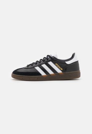 Musta Adidas Spezial -lenkkari, jossa valkoiset raidat, kumipohja, mustat nauhat ja kultainen "Spezial"-teksti sivulla.