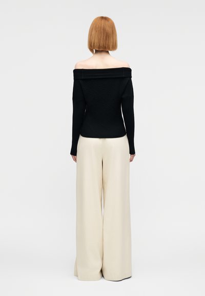 Μαύρο ριμπ πουλόβερ με ανοιχτούς ώμους και μακριά μανίκια, σε συνδυασμό με μπεζ παντελόνες φαρδιάς γραμμής. Ομαλή υφή και διαγώνιο μοτίβο στο πουλόβερ.