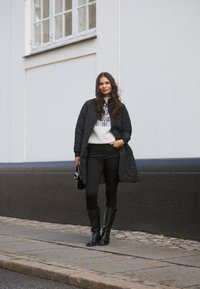 Black quilted coat over a light sweater with a geometric pattern, black pants, and knee-high black boots, paired with a small black handbag.
