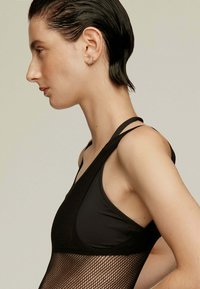 Bodysuit negro con una superposición de malla, diseño elegante y tirantes finos. Textura suave con secciones abiertas que contrastan con la tela sólida.