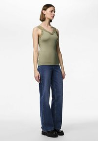 Olivenfarget tank topp med blonder langs halsen, kombinert med løse blå denimjeans og svarte platåsko.