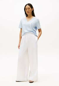 Jasnoniebieska bawełniana koszulka z dekoltem w serek zestawiona z białymi spodniami o szerokich nogawkach. Spodnie mają elastyczny pas i gładką fakturę. Czarne sandały.