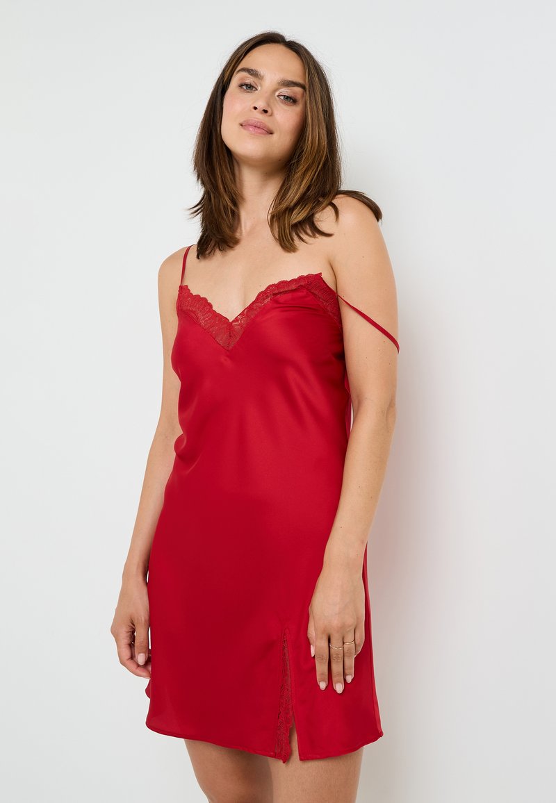 Pigiamino rosso in satin con bordo in pizzo sul collo e spacco laterale. Presenta spalline sottili e regolabili e una texture liscia e lucida.