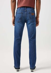 Niebieskie dżinsy o prostym kroju nogawki, z dwiema tylnymi kieszeniami ozdobionymi zygzakowym przeszyciem oraz brązową skórzaną naszywką na pasku.