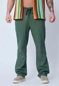 Pantalons en coton vert à coupe décontractée avec une taille à cordon, accompagnés d'une chemise rayée colorée et de chaussures gris-chaussons.