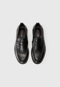 Sorte skinnslippers med en glatt tekstur, med en sydd søm og diskret merkeområde inni. Rund tå og lav profil såle.