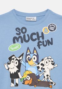 Svetlo modra majica s kratkimi rokavi, ki prikazuje risane pse. Besedilo pravi "TOLIKO ZABAVE." Vsebuje tudi nalepke z napisi "vedno dobre čase" in "Vzemi to na maksimum, Bluey."