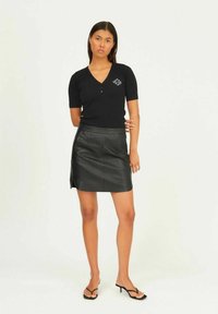 Black short-sleeve V-neck shirt with button detail paired with a black leather mini skirt. The outfit features a smooth texture and minimalistic design.